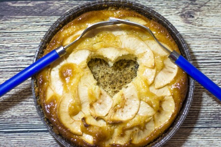 Apple pie with a hollow heart-shaped and two forks entwined on a wooden tableの写真素材