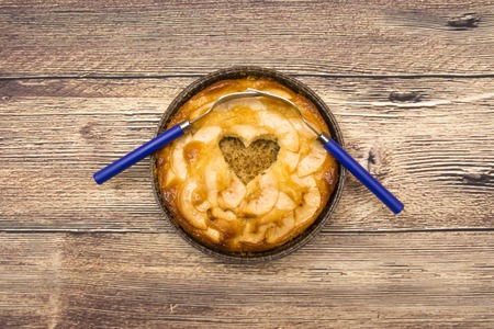 Apple pie with a hollow heart-shaped and two forks entwined on a wooden tableの写真素材