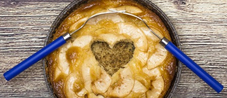 Apple pie with a hollow heart-shaped and two forks entwined on a wooden tableの写真素材