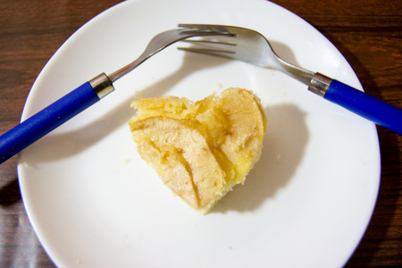 Piece of apple pie with heart shape and two forks interlaced on a wooden tableの写真素材