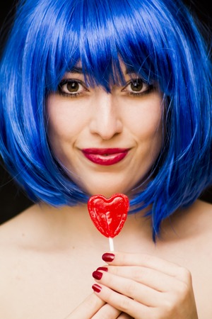 Beauty Woman With Blue Wig And Sunglasses and holding with her hand a candy with heart shape Portrait Isolated over Black Backgroundの写真素材