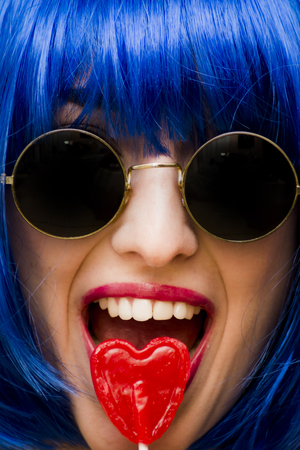 Beauty Woman With Blue Wig And Sunglasses and holding with her hand a candy with heart shape Portrait Isolated over Black Backgroundの写真素材
