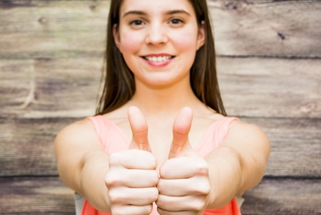 Portrait of a beautiful woman with her thumb up in sign of optimism on wooden backgroundの写真素材