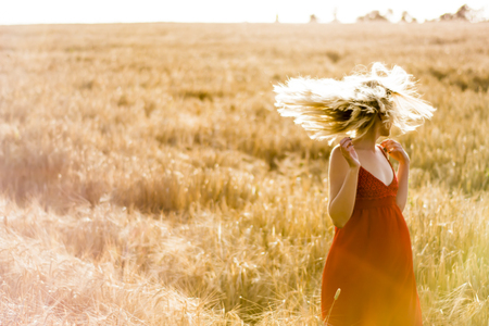 Beautiful blond woman in a red dress, on a wheat field at sunsetの写真素材