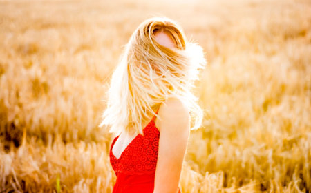 Beautiful blond woman in a red dress, on a wheat field at sunsetの写真素材