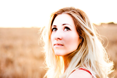 Beautiful blond woman in a red dress, on a wheat field at sunsetの写真素材