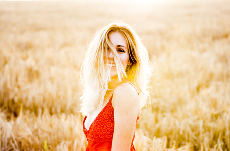 Beautiful blond woman in a red dress, on a wheat field at sunsetの写真素材