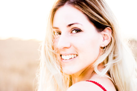Beautiful blond woman in a red dress, on a wheat field at sunset