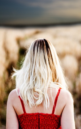 Beautiful blond woman in a red dress, on a wheat field at sunsetの写真素材