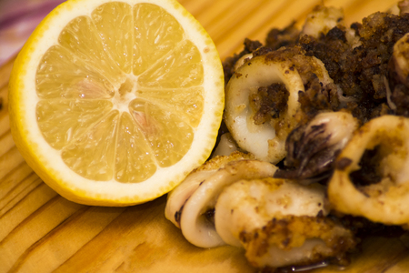 Fried squids and shipirons  with lemon on a wooden plateの写真素材