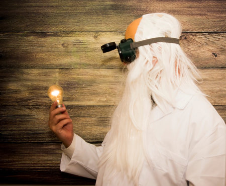 Crazy scientist elderly man holding an inexplicably lit bulb with some strange glasses on wooden...