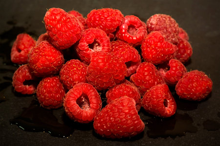 Lot of delicious raspberries on black stone