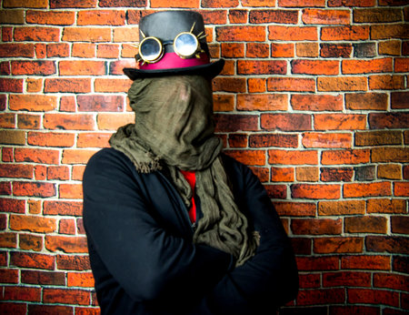 Steampunk man with hidden face, hat and glasses on background of vintage brick wall