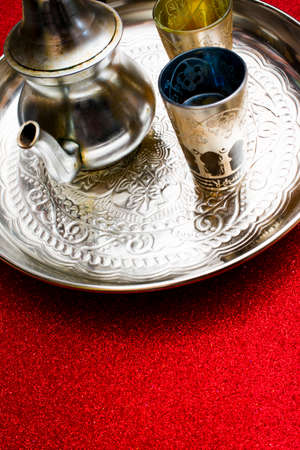 Group of teapot and glasses of oriental tea on a tray on red background with glitterの写真素材