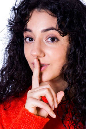 Portrait of a beautiful woman with red sweater commanding silence on white backgroundの写真素材