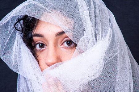 Portrait of a beautiful woman with white veil on black backgroundの写真素材