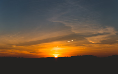 Sun is going down below trees in the horizonの写真素材
