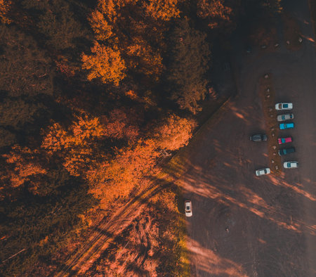 View from the air of a gravel parking lot at the side of a forest in autumn when the sun is going...