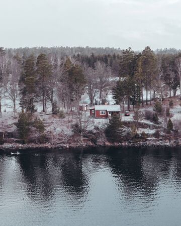 View from the Stockholm archipelago with snow on the ground with a house in the woods and water that reflects, Swedenの写真素材