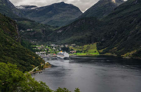 Geiranger fjord seen from the hillside on summer day with one cruise ship in port and the tall mountains behind, Norwayの写真素材
