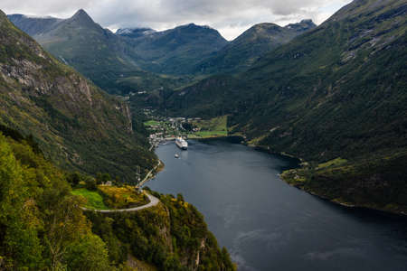Majestic and big Geiranger fjord with sun peaking from behind the dark clouds on a late summer dayの写真素材