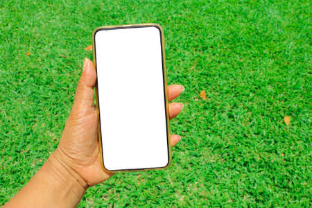 Hand keeping cell phone blank screen with green grass backgroundの写真素材