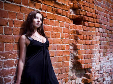 Charming young woman in black dress near the brick wallの写真素材