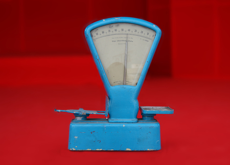 Old worn blue weighing scale on red background, souvenir of the communism era in Polandの写真素材