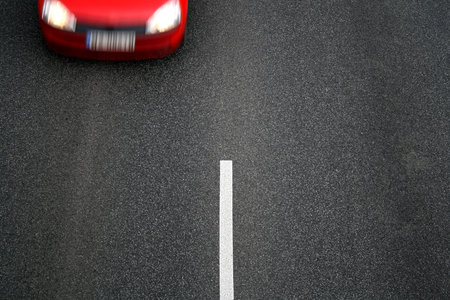 Background of black tarmac of street with motion blurred front of red car and white stripe in the...