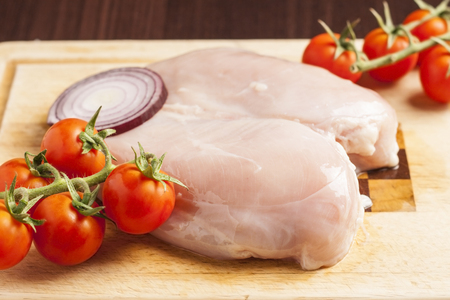 Fresh raw chicken breast on cutting board with cocktail tomatoの写真素材
