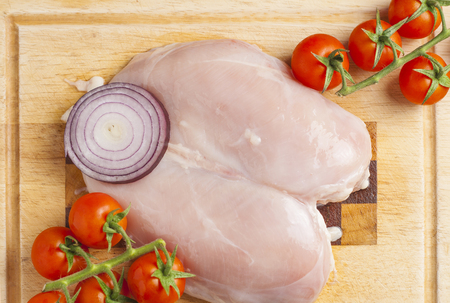 Fresh raw chicken breast on cutting board with cocktail tomatoの写真素材