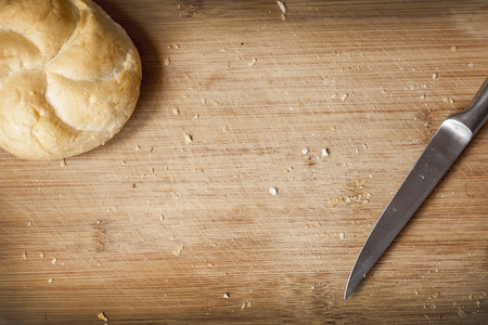Kaiser roll and kitchen knife on cutting board with crumbsの写真素材