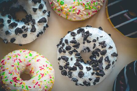 Flat lay image of donut with white glaze and black cookies amids other different donutsの写真素材