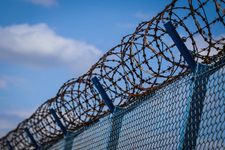 Barbed wire on top of metal mesh netting fence enclosing airport against cloudy sky