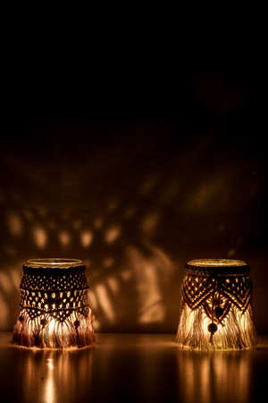 Macrame hand woven with cord two lanterns glow making abstract shadow patterns on the wallの写真素材