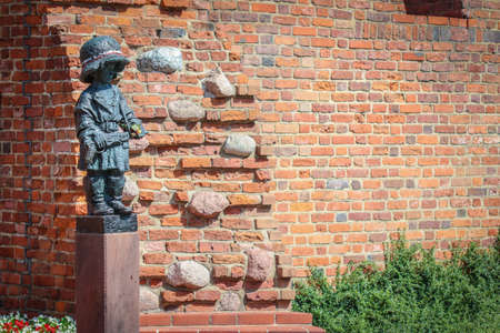 Monument of little boy insurgent in oversized german helmet and boots, participant of Warsaw Uprising in 1944 against red brick of medieval city wallsのeditorial素材