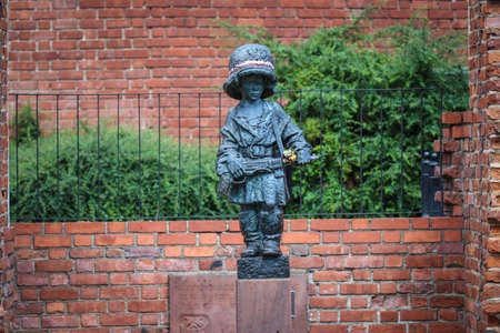 Monument of little boy insurgent in oversized german helmet and boots, participant of Warsaw Uprising in 1944 against red brick of medieval city wallsの写真素材