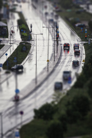 Cars wait on red traffic light on wet and shining street during rain, image with tilt shift effect...