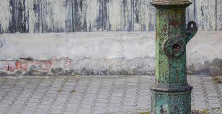 Very old warn green out of order street water pump standing alongside pavement with copy spaceの写真素材