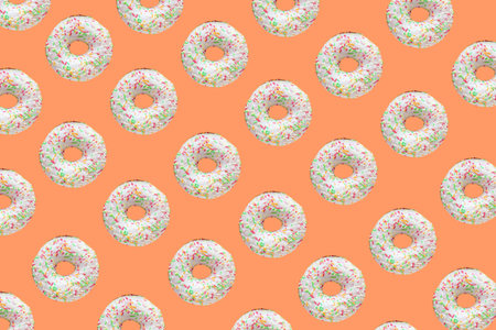 Pattern made of ring donuts with white glaze and clourful hundreds and thousands on orange...
