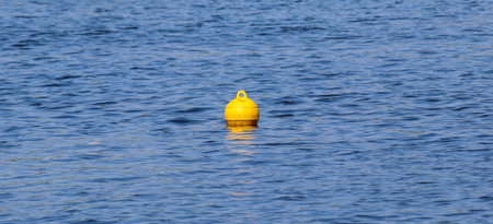 Yellow floating buoy ball on water surface marks boundary of safe swimming areaの写真素材