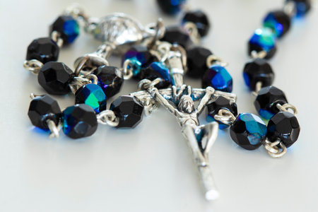 Macro close-up on rosary lying on white table, focus on Jesus Christ on the crossの写真素材