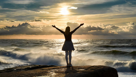 Silhouette of Woman standing backward on the rock with outstretched arms enjoying the breeze from the seaの写真素材