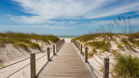 A serene wooden pier stretches into the tranquil ocean with a sunny sky above and puffy clouds.の写真素材