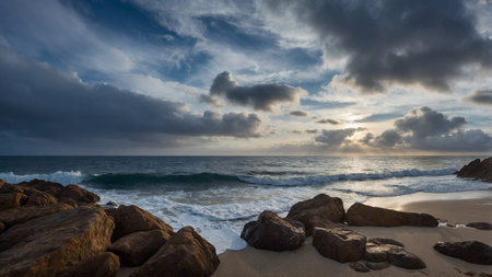 This serene landscape image captures the contrast between the sunlight piercing through heavy clouds and the rhythmic ocean waves crashing onto a pristine, sandy beach, creating a peaceful yet dramatic scene. AI generated imageの写真素材