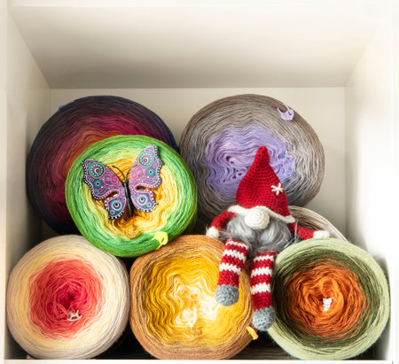 Gradient yarn cakes arranged in a white shelf, featuring a christmas gnome and a butterfly decoration, perfect for knitting and crochet projectsの写真素材