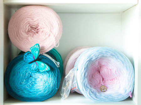 Colorful yarn cakes, adorned with a butterfly decoration, sit on a shelf, ready for knitting or crochet projectsの写真素材