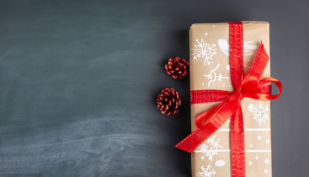 Gift box with red ribbon and pine cone on blackboard backgroundの素材