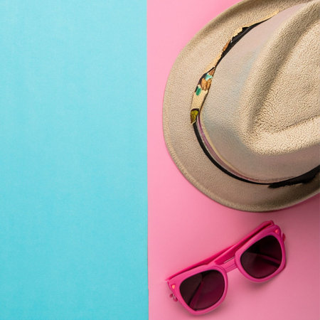 Beach hat and sunglasses on pink and blue background. Top viewの素材