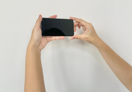 Woman hands holding smart phone with blank screen on white wall background.の写真素材